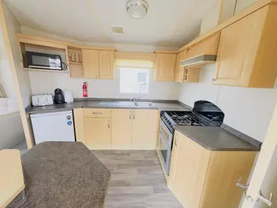 a small kitchen with wooden cabinets and a stove at Santos Caravan Beautiful Holiday Home in Clacton-on-Sea