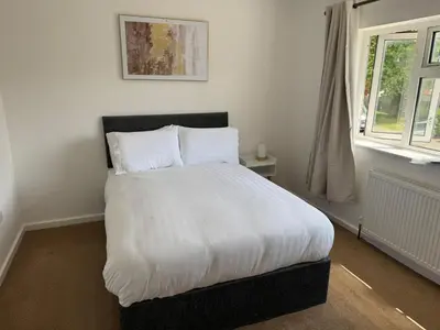 a bedroom with a bed with white sheets and a window at Holly Copse in Stevenage