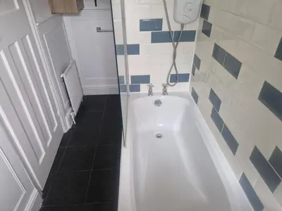 a white bath tub in a bathroom with blue and white tiles at 1930s conversion two apartment in Harold Wood