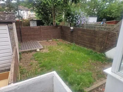 a backyard with a fence and a bench and grass at 1930s conversion two apartment in Harold Wood
