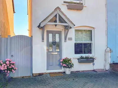 a white house with a blue door and a window at Lavender Cottage in Frinton-on-Sea