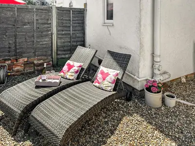 a wicker bench with two pillows on a patio at Lavender Cottage in Frinton-on-Sea