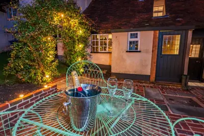 a table with wine glasses on it in front of a house at Cosy & charming medieval 'Bumble Cottage' in Kersey