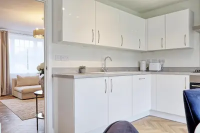 a kitchen with white cabinets and a living room at Luxury and cosy 2 bed entire house in Essex 20 mins from beach in Colchester