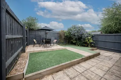 a garden with a patio with chairs and an umbrella at 15 Mins to Sizewell C - Driveway Parking - Contractor Friendly - 2 Bedroom in Saxmundham