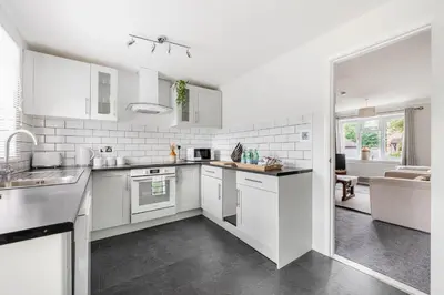 a white kitchen with white appliances and a living room at 15 Mins to Sizewell C - Driveway Parking - Contractor Friendly - 2 Bedroom in Saxmundham