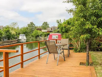 a wooden dock with a table and chairs on a river at Kingfisher in Ely
