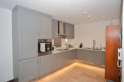 a kitchen with white cabinets and a wooden floor at Seaview City Lodge , 2- bedroom flat with Parking in Southend-on-Sea