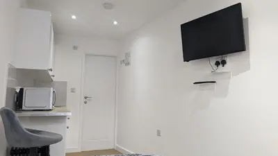a white room with a chair and a tv on the wall at The Southend Airport Lodge in Southend-on-Sea