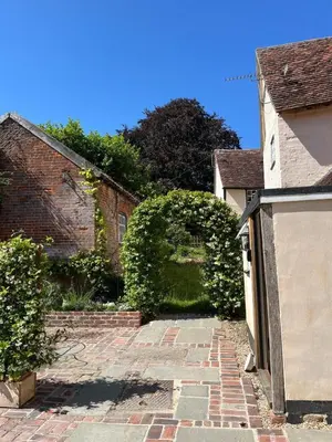 a brick walkway leading to a building with a hedge at Taper House - Cosy Medieval Cottage in Kersey
