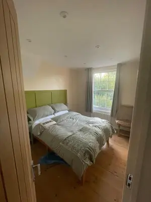 a bedroom with a bed with a green headboard and a window at Cottage of Content in Wivenhoe