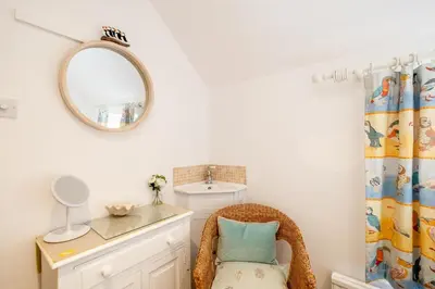 a wicker chair in a bathroom with a mirror at Seahorse Cottage, Aldeburgh - sleeps 4 - Adult only property - Managed by Aldeburgh Coastal Cottages in Aldeburgh