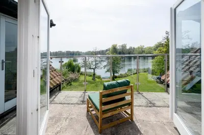 a wooden bench sitting on a patio with a view of the water at Claysmead - A large Lakeside House in Thorpeness - Aldeburgh Coastal Cottages in Thorpeness