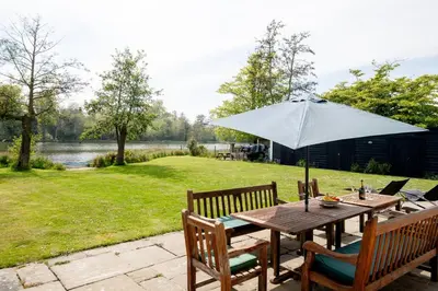 a wooden table with an umbrella on a patio at Claysmead - A large Lakeside House in Thorpeness - Aldeburgh Coastal Cottages in Thorpeness