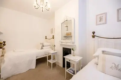 a white bedroom with two beds and a fireplace at La Ronessa, Aldeburgh in Aldeburgh