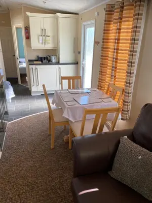 a living room with a table and chairs and a kitchen at Hadleigh Caravans at Seawick Clacton in Clacton-on-Sea