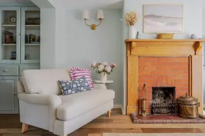 a living room with a chair and a fireplace at Boutique Suffolk Cottage Cosy Family Holiday Home with Garden Near Aldeburgh in Kettleburgh