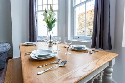 a wooden table with plates and glasses and a vase of flowers at Stylish & Modern Home by the Sea Near Three Shells in Southend-on-Sea