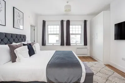 a bedroom with a large bed and two windows at 3 Bed Apartment with Balcony in Southend on Sea! in Southend-on-Sea