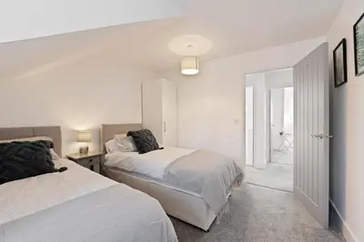 a white bedroom with two beds and a hallway at Modern town centre apartment in Bishops Stortford
