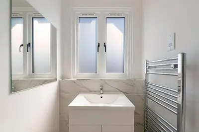 a white bathroom with a sink and two windows at Modern town centre apartment in Bishops Stortford