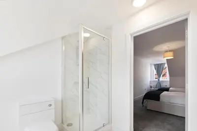 a white bathroom with a shower and a bedroom at Modern town centre apartment in Bishops Stortford