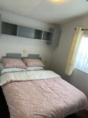 a bedroom with a bed with a pink comforter and a window at Seawick holiday park caravan in Saint Osyth