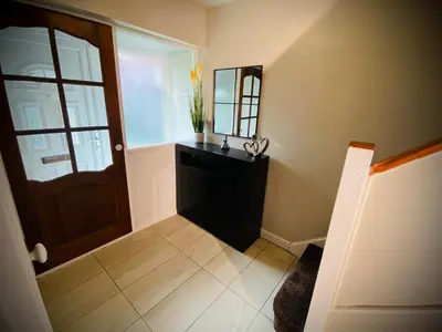 a hallway with a mirror and a black dresser and a door at Modern-PetFriendly-privateGarden-Family-20MinToLDN in Stevenage