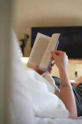 a woman laying in bed reading a book at The Lodges - Waresley Park Estate