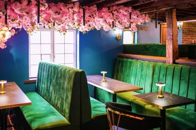a restaurant with green booths and tables and pink flowers at The Courtyard Lodge in Hitchin