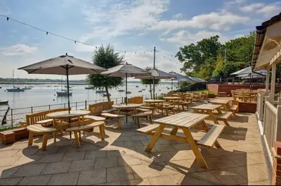 a row of tables and benches with umbrellas next to the water at A Beautiful Country Cottage in Waldringfield
