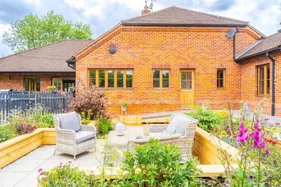 a brick house with two chairs and a table in a garden at Large indoor swimming pool in Thetford Forest - The Pool House in Downham