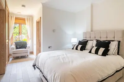 a white bedroom with a large bed and a chair at Large indoor swimming pool in Thetford Forest - The Pool House in Downham