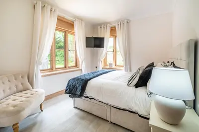 a bedroom with a bed and a chair and window at Large indoor swimming pool in Thetford Forest - The Pool House in Downham