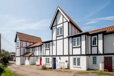 a white and black house with a red door at 3 Bell Lodge - near Thorpeness Country Club and the beach - Aldeburgh Coastal Cottages in Thorpeness