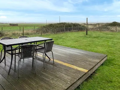 a table and chairs on a deck with a field at Humperdink in Saint Osyth