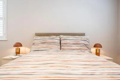 a bed with a striped comforter and two lamps at Goldfinch, Leiston in Leiston
