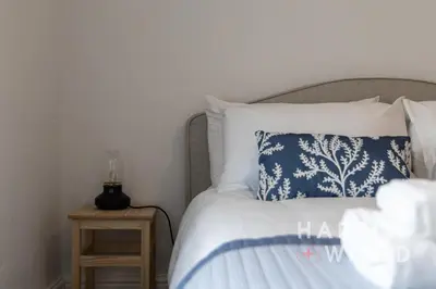 a bed with a blue and white pillow and a side table at Saltmarsh Cottage in Brightlingsea
