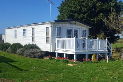 a small white house with a porch and a yard at Sunny corner caravan in Saint Osyth