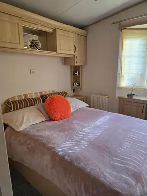 a bedroom with a large bed with an orange pillow on it at Sunny corner caravan in Saint Osyth