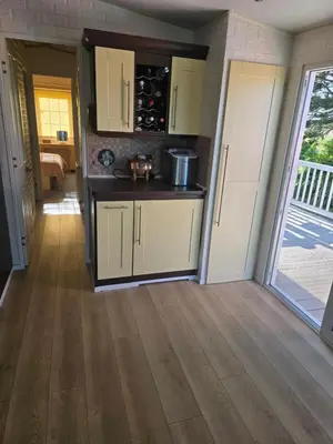 a kitchen with white cabinets and a wooden floor at Sunny corner caravan in Saint Osyth