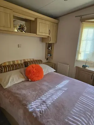 a bed with an orange pillow on top of it at Sunny corner caravan in Saint Osyth
