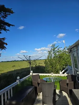 a patio with chairs and a table and a field at Sunny corner caravan in Saint Osyth