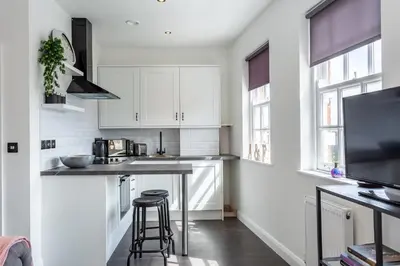 a kitchen with white cabinets and a counter with stools at Central Studio Flats with Parking in Southend on Sea in Southend-on-Sea