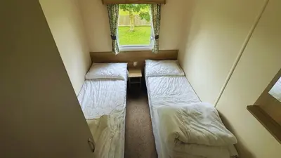 two beds in a small room with a window at Sunny Beach Holidays Home in Jaywick Sands