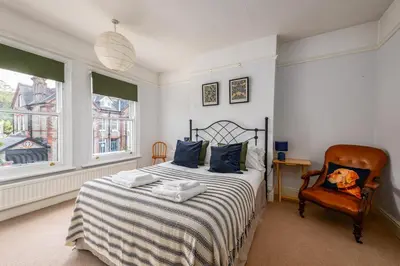 a bedroom with a bed and a chair and two windows at Elegant Period House in the Historic Heart of Cambridge - sleeps 12 in Cambridge