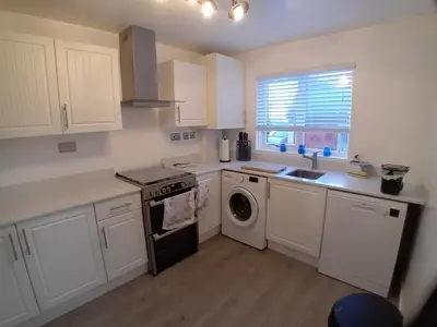 a kitchen with white cabinets and a washer and dryer at 'Ks' Yard in Great Dunmow