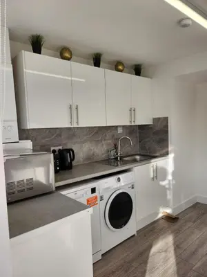 a kitchen with white cabinets and a washing machine at Ensuite deluxe home in Basildon