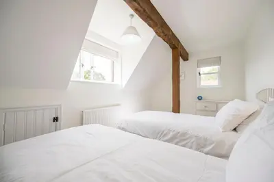 two beds in a white room with two windows at Hollybank Cottage, Ufford in Ufford