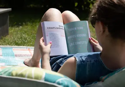 a woman sitting on a blanket reading a book at Sycamore Lodge with Hot Tub- Quirky & Romantic in Halstead